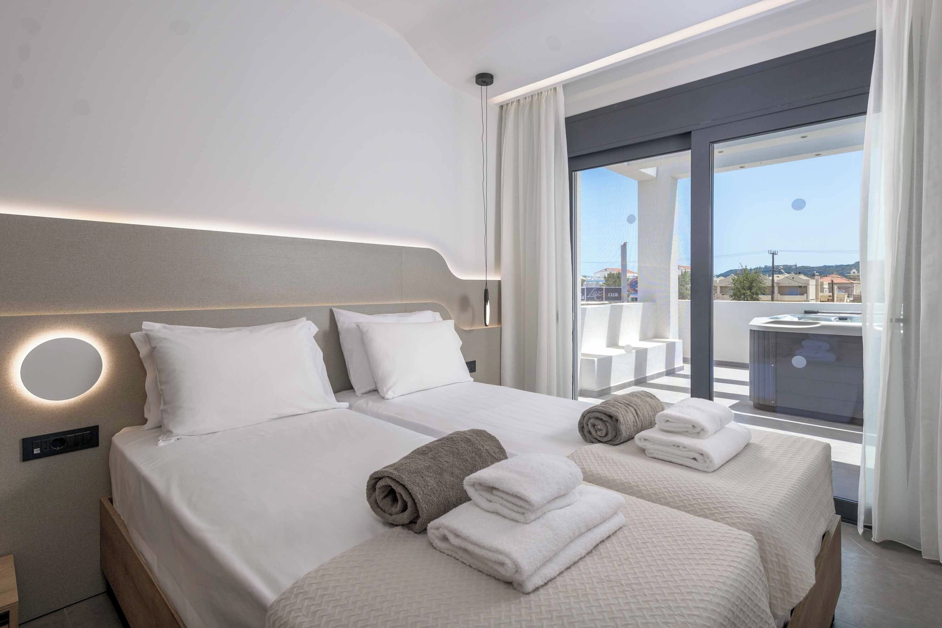 A modern hotel room with two beds, a large window, and a view of the city.