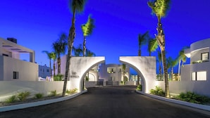 A modern hotel entrance with a white facade, palm trees, and a clear blue sky.