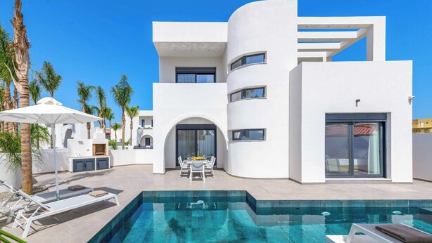 A modern multi-story building with a swimming pool, outdoor seating, and palm trees.
