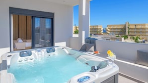 A modern outdoor hot tub with a control panel, a glass door leading to a room, and a balcony with a view of a cityscape.