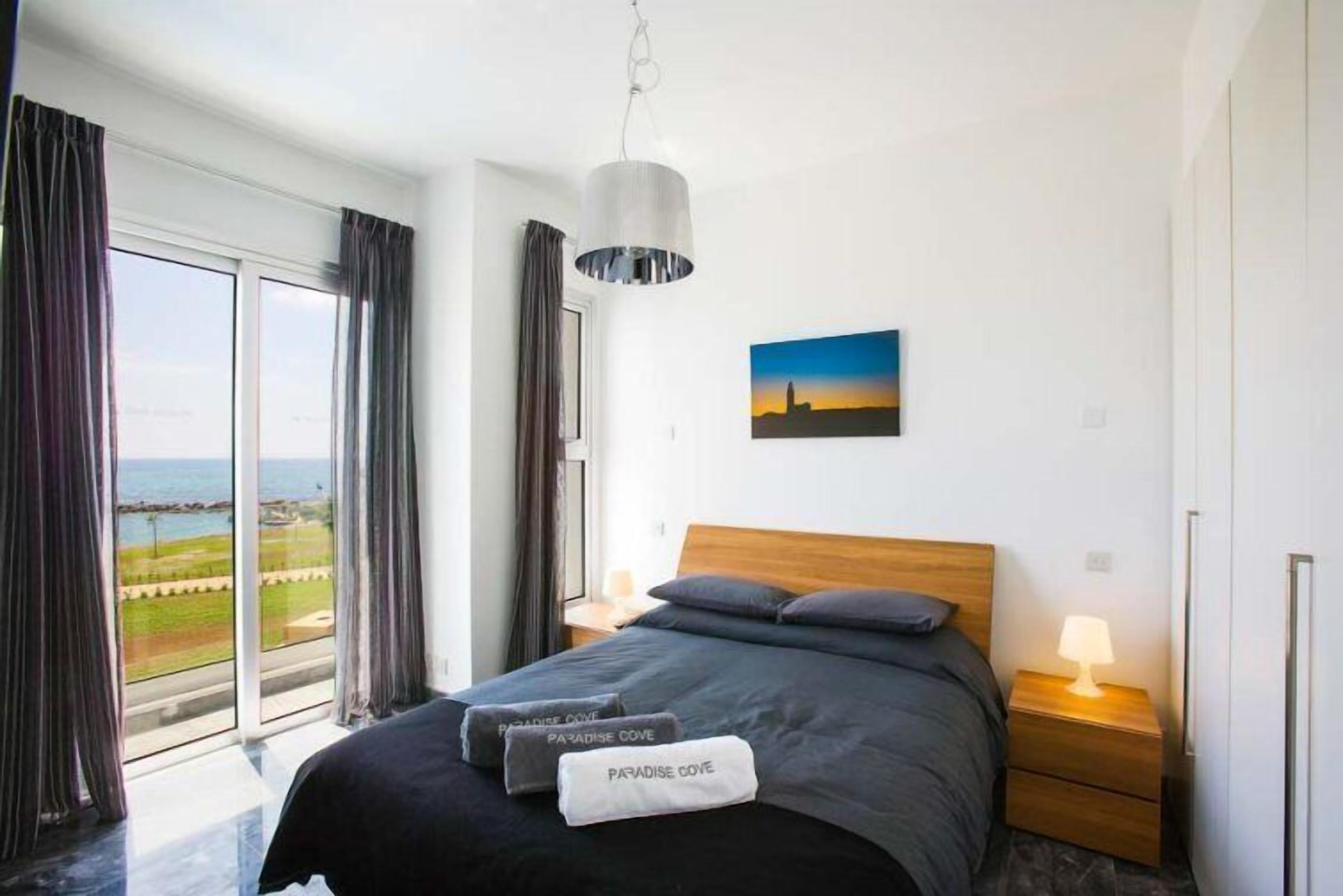 Una habitación de hotel moderna con una cama grande, vistas al mar y un cuadro en la pared.