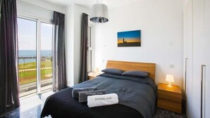A modern hotel room with a large bed, a view of the sea, and a painting on the wall. - Villa Cyan Paphos - Three Bedroom Villa, Sleeps 6 (Pafos)