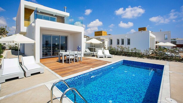 Un área moderna junto a la piscina con una piscina azul cristalina, sillas de descanso blancas y una terraza de madera.