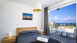 Un dormitorio moderno con una cama grande, vistas al mar y un balcón con mobiliario.