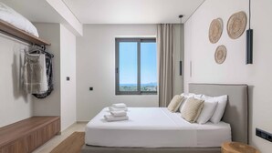A modern bedroom with a large bed, a wooden bench, a window with a view, and decorative wall art. - Massari Hills Villa 8 (Rhodes)