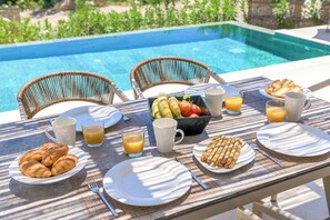 A breakfast setup by a pool with croissants, fruit, and juice.