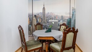 Un comedor con una mesa y cuatro sillas, vistas a un paisaje urbano a través de ventanas amplias y suelo de madera.
