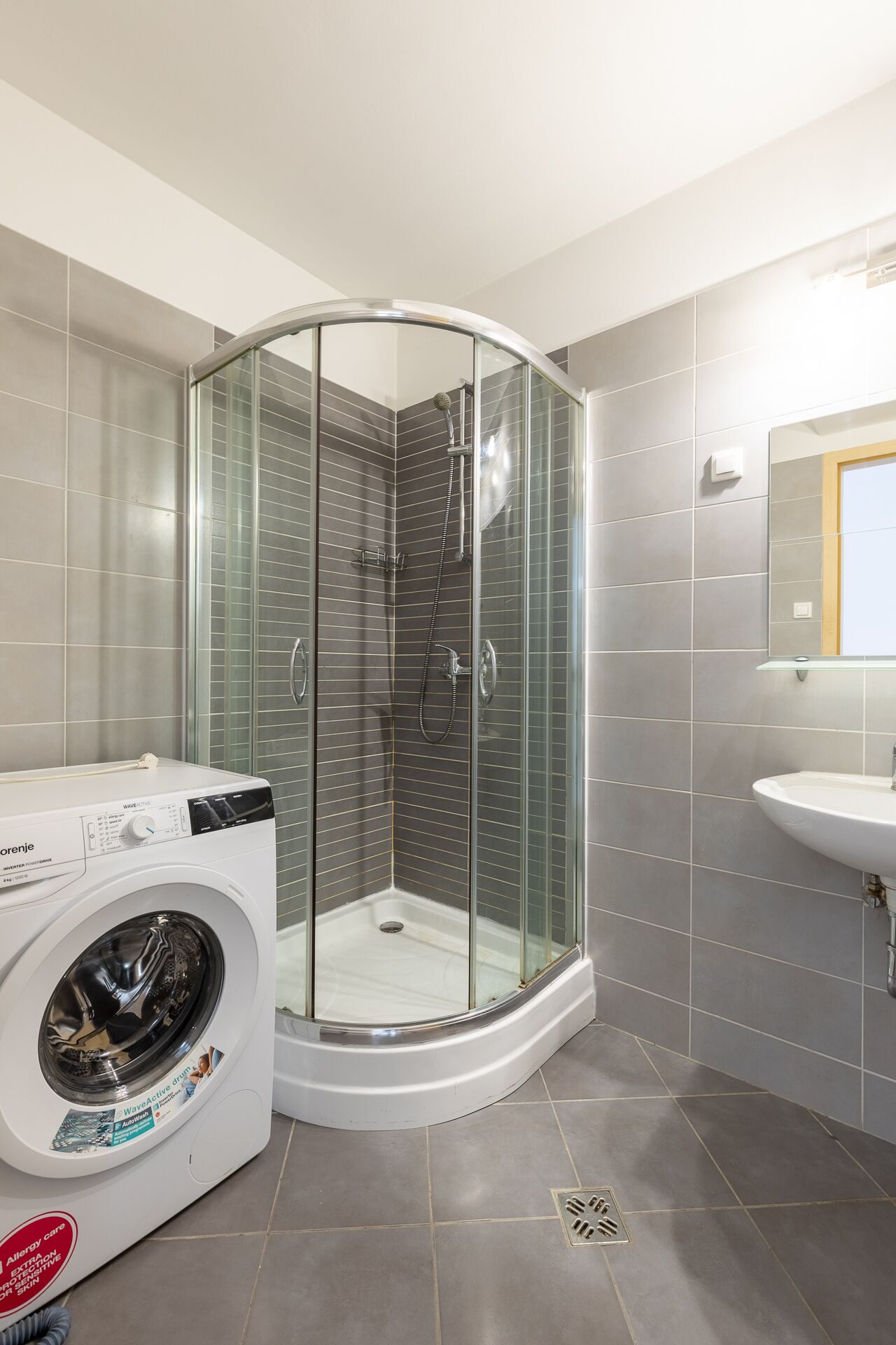 A modern bathroom with a glass-enclosed shower, a built-in washing machine, and a sink.
