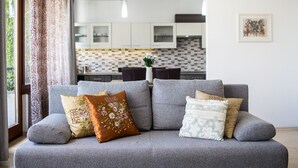 Una sala de estar moderna con un sofá gris, cojines estampados y una vista de una cocina al fondo.