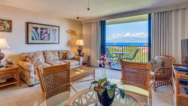 A hotel room with a balcony, a sofa, a coffee table, and wicker furniture.