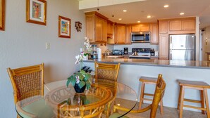 A modern kitchen with wooden cabinets, a stainless steel refrigerator, and a glass dining table with wicker chairs.