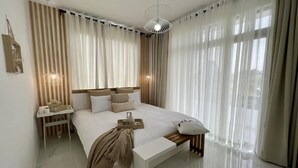 Un dormitorio moderno con una cama grande, mesitas de noche, un banco y cortinas de gasa.