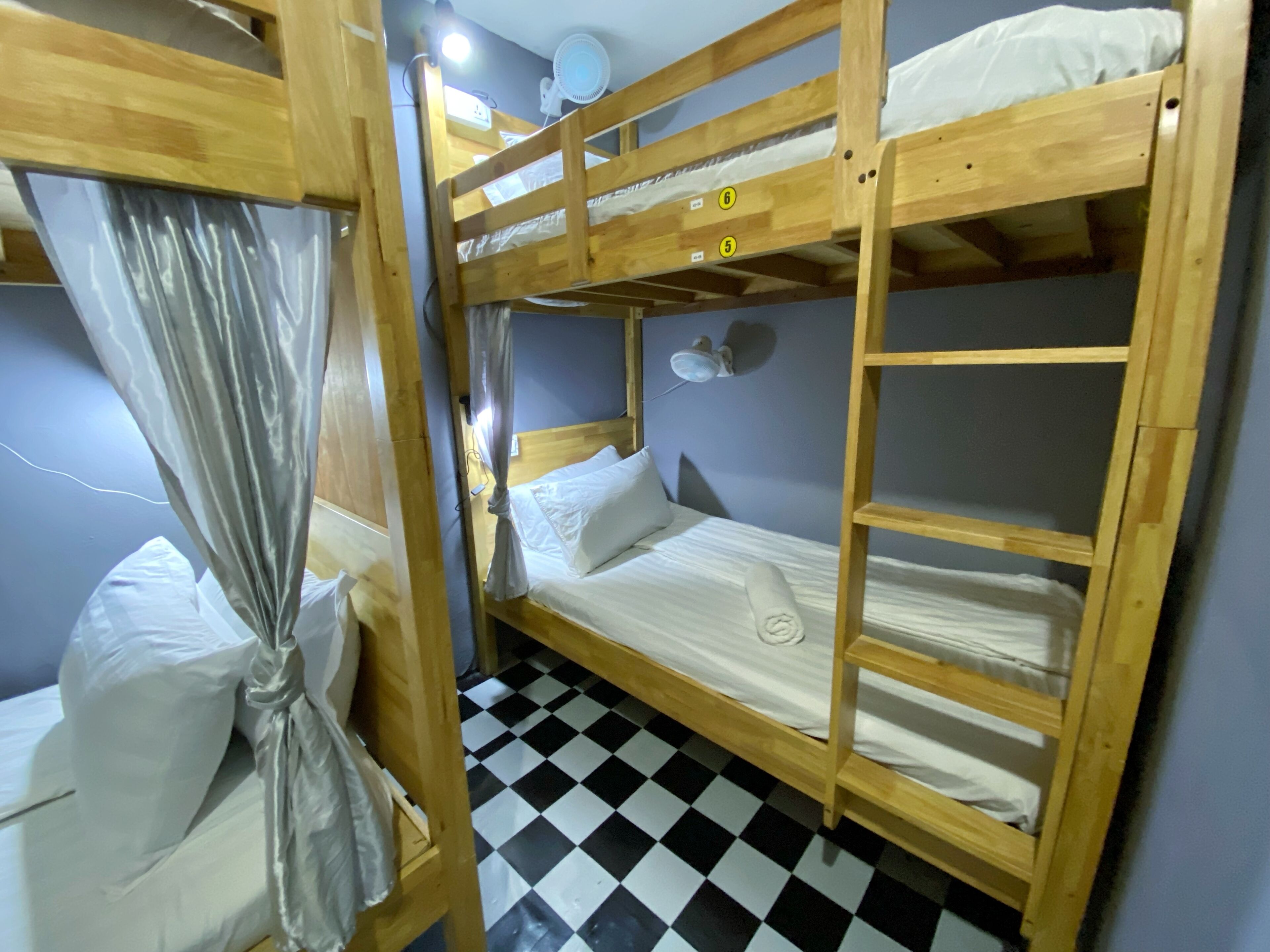 A bunk bed room with a checkered floor, a curtain, and a wall-mounted fan.