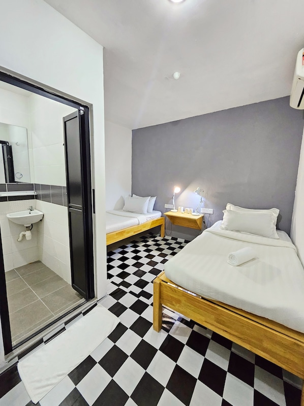 Habitación de hotel con piso a cuadros, una cama, una mesita de noche con lámpara, un lavamanos pequeño y un espejo.