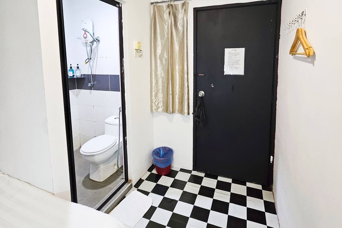 A bathroom with a black and white checkered floor, a toilet, a shower, and a door with a notice on it.