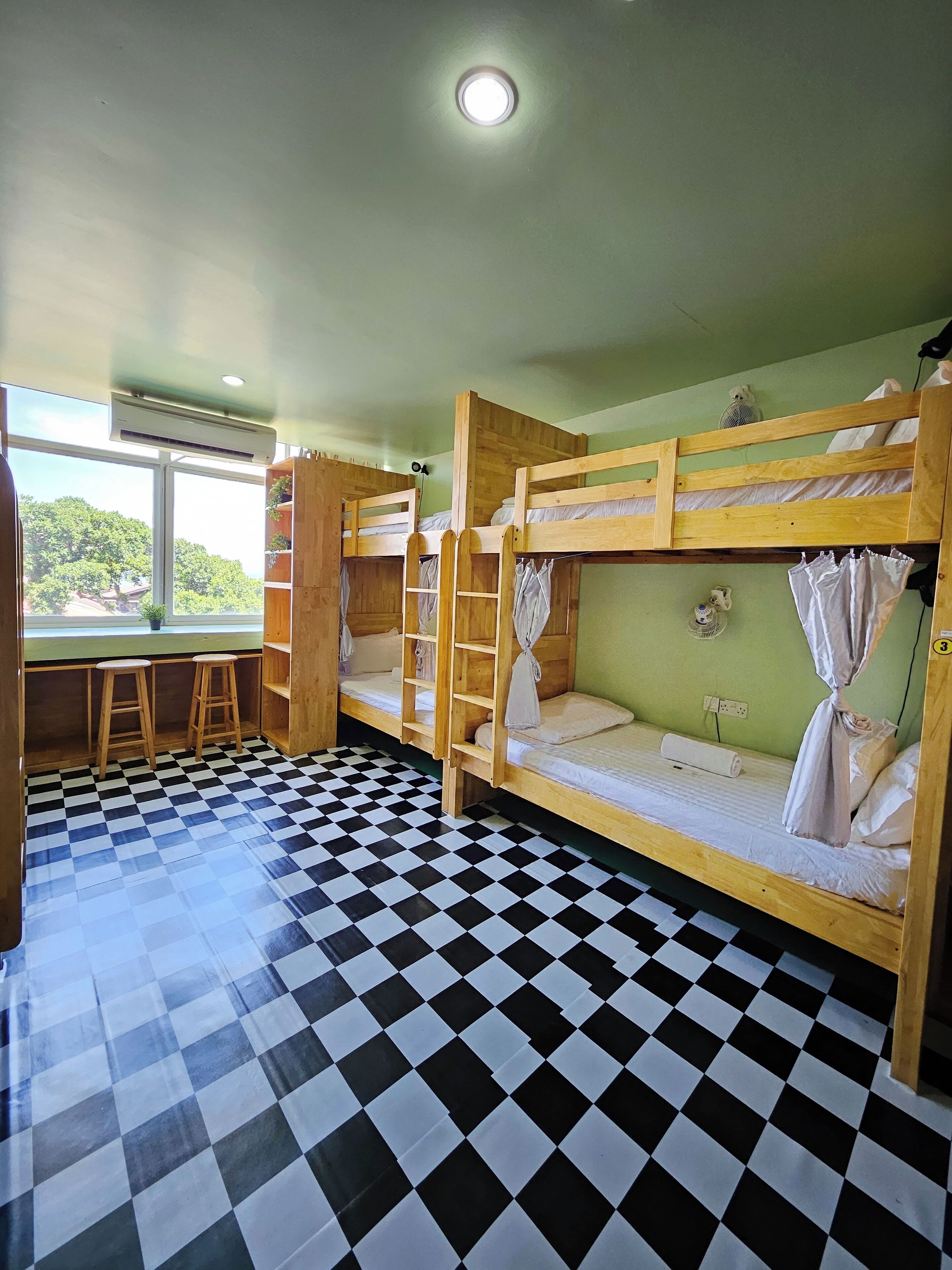 A room with bunk beds, a checkered floor, a window with a view, and a small desk with stools.