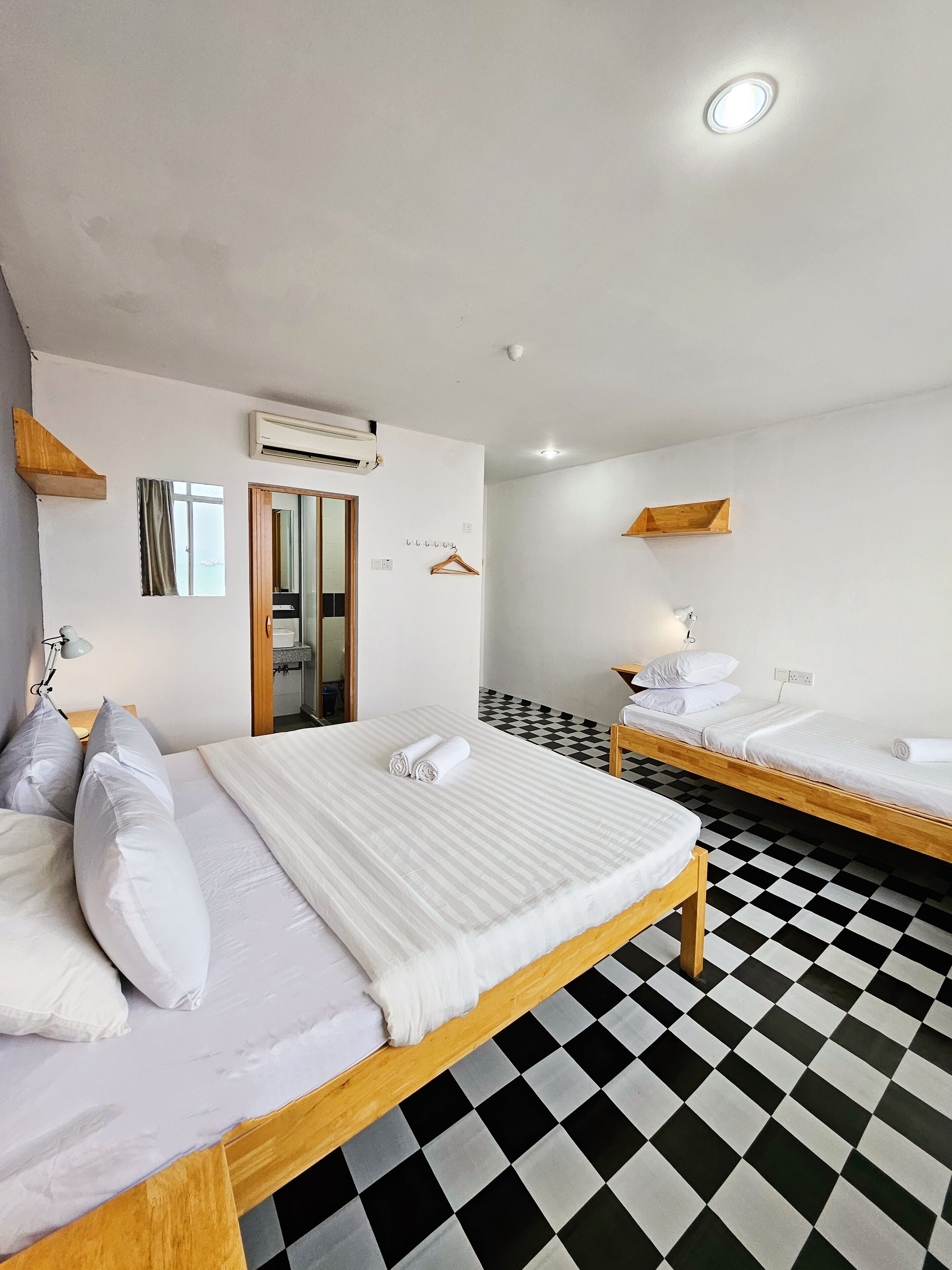 A hotel room with two beds, a checkered floor, a mirror, a hanging light, and a window with curtains.
