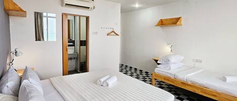 A hotel room with two beds, a checkered floor, a mirror, a hanging light, and a window with curtains.