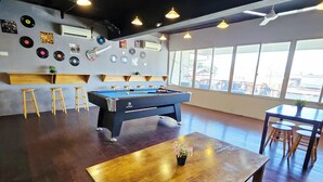 A pool table in a room with wooden flooring, a ceiling fan, and a window with a view of the outside. - The 60 (George Town)