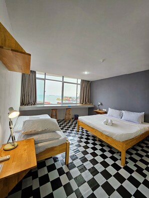 Habitación de hotel con dos camas, piso a cuadros, un ventanal con vistas y un escritorio con lámpara.