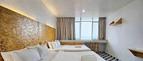 A hotel room with a checkered floor, a large bed with white linens, a wooden headboard, a window with curtains, and a small wooden shelf.