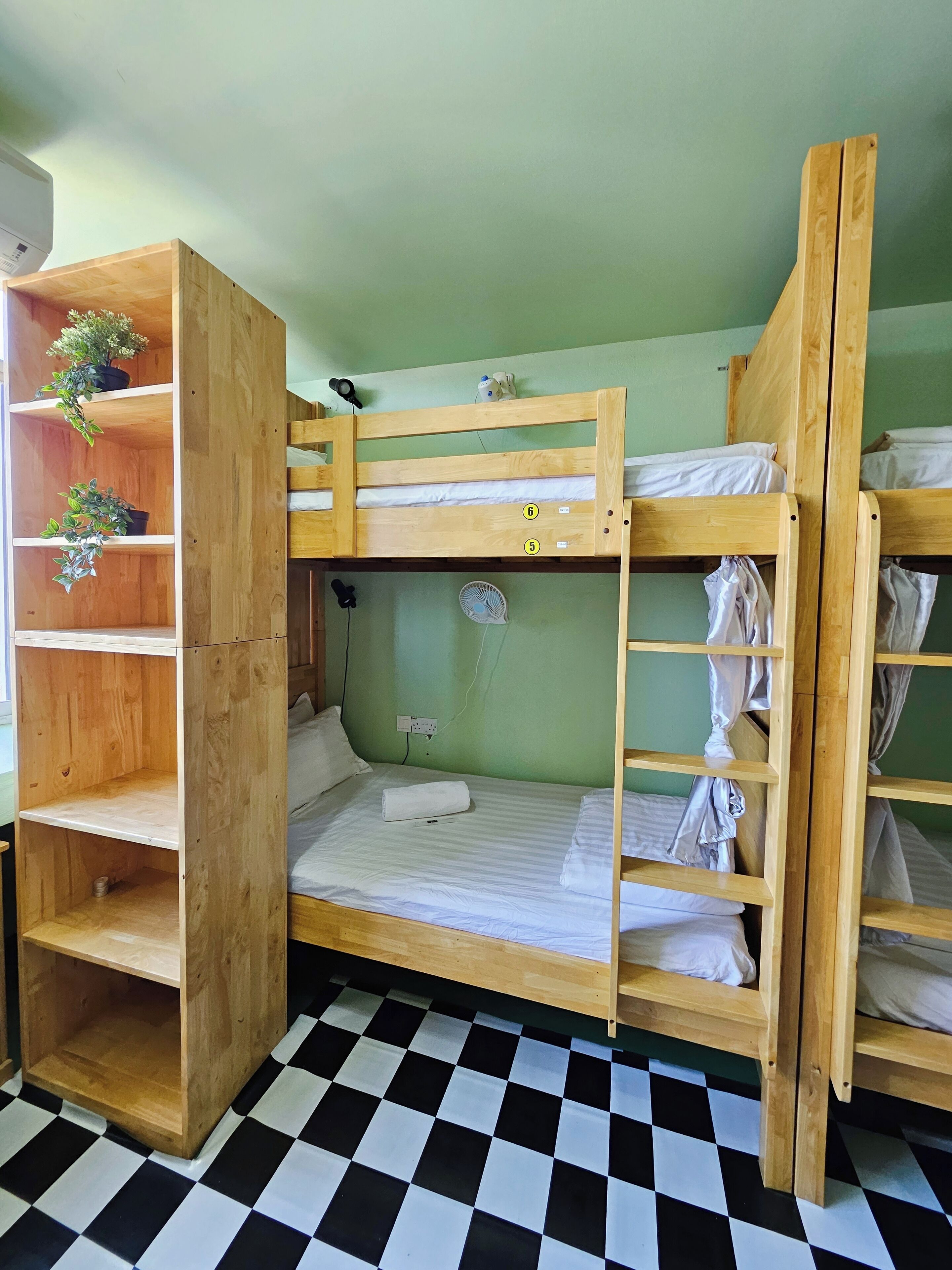 A bunk bed room with a checkered floor, wooden shelves with plants, and a power outlet on the wall.