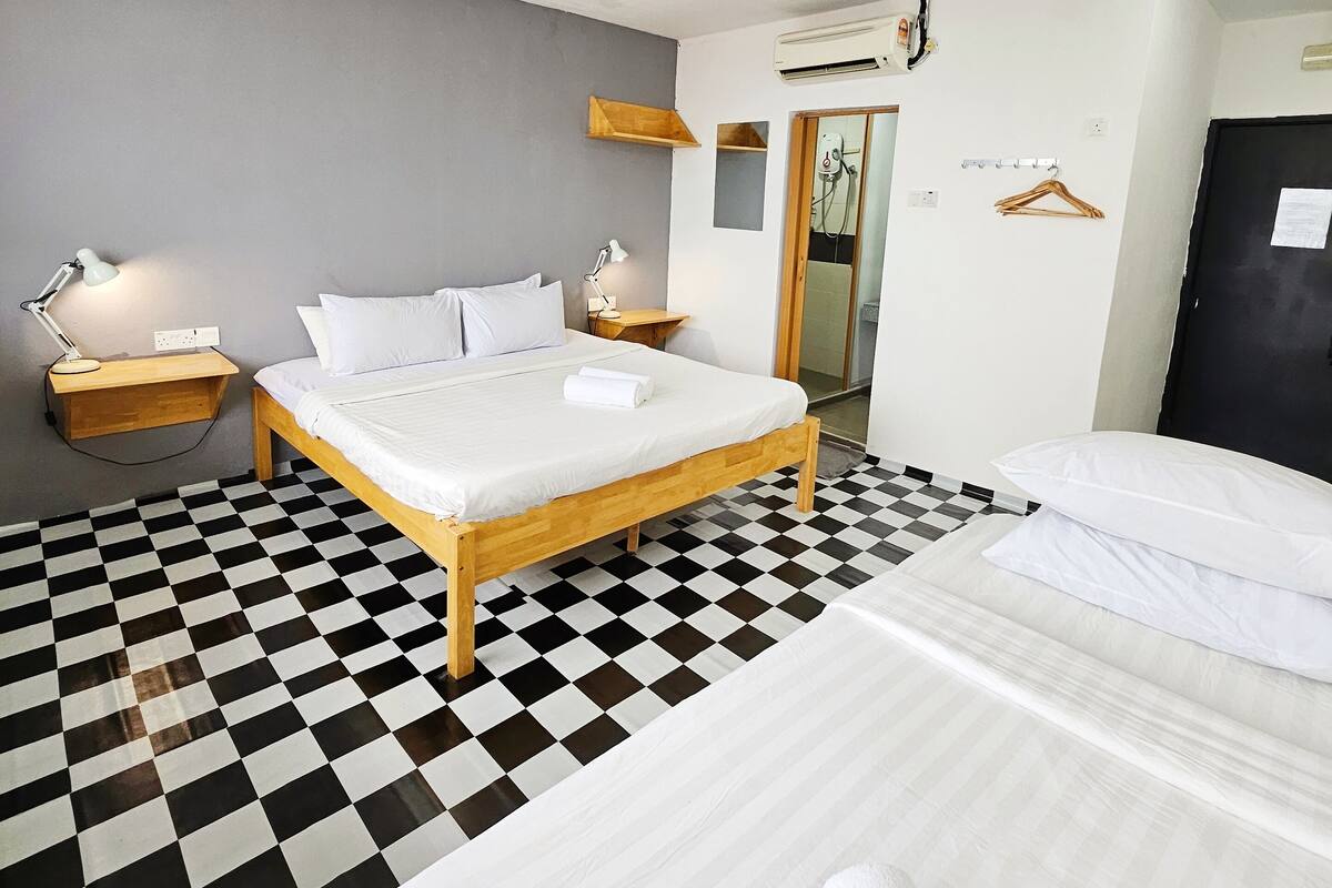 A hotel room with two beds, checkered flooring, a wooden headboard, bedside tables with lamps, and an air conditioning unit.