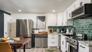 A modern kitchen with stainless steel appliances, white cabinetry, and a green tiled backsplash.