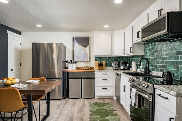 A modern kitchen with stainless steel appliances, white cabinetry, and a green tiled backsplash.