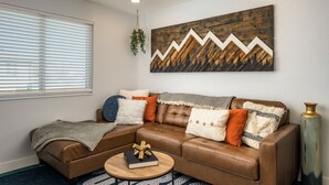 A living room with a brown leather sectional sofa, a round coffee table, and a large abstract painting on the wall. - Modern 2BR Denver Retreat w/ King Beds + Full Kitchen Near Arvada & Downtown! (Denver)