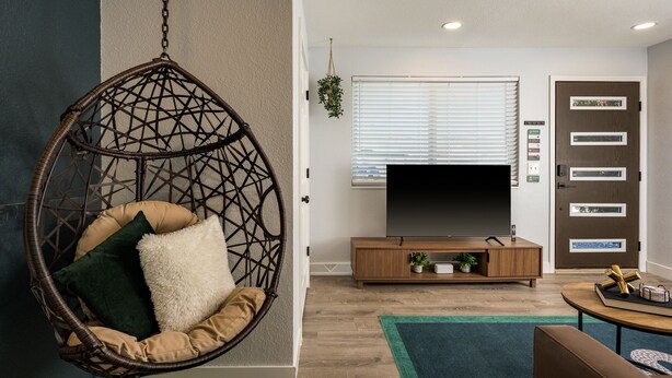 A living room with a hanging chair, a flat-screen TV, a wooden cabinet, and a door with a control panel. - Modern 2BR Denver Retreat w/ King Beds + Full Kitchen Near Arvada & Downtown! (Denver)