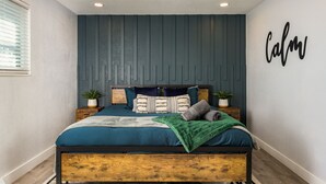 A bedroom with a bed, pillows, a green blanket, and a 'Calm' wall art. - Modern 2BR Denver Retreat w/ King Beds + Full Kitchen Near Arvada & Downtown! (Denver)
