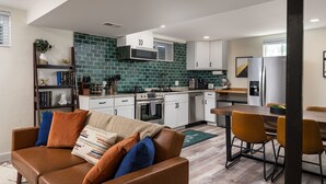 A modern kitchen with white cabinets, a green backsplash, and a dining area with a wooden table and chairs. - Stylish 1BR King Bed Garden Level Denver Retreat, w/ Full Kitchen Near Downtown (Denver)