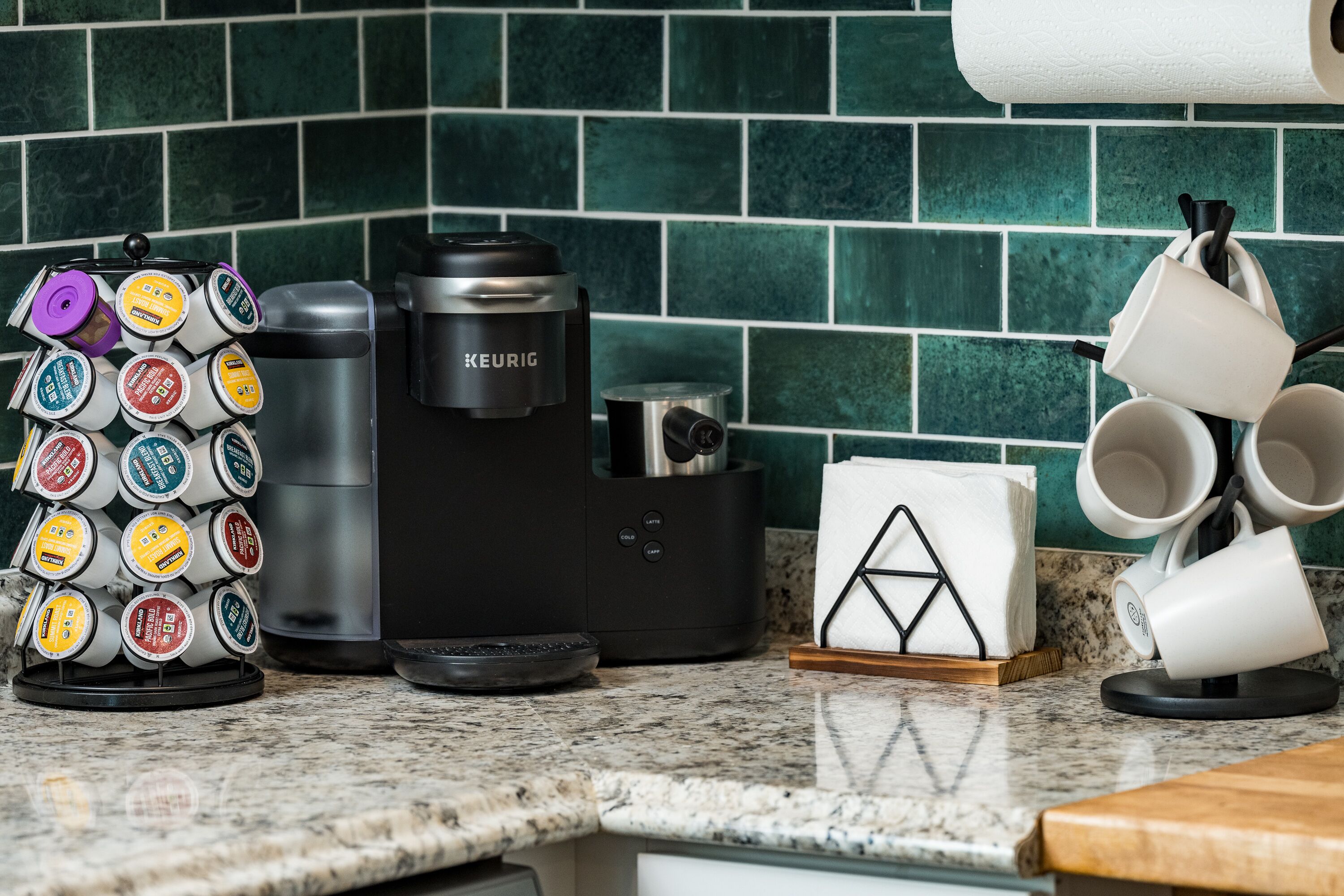 A coffee maker, a coffee pod holder, and a stack of white mugs on a kitchen counter.