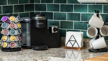A coffee maker, a coffee pod holder, and a stack of white mugs on a kitchen counter.