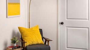A room with a chair, a small table with a plant and books, a yellow cushion, a floor lamp, and a door. - Stylish 1BR King Bed Garden Level Denver Retreat, w/ Full Kitchen Near Downtown (Denver)