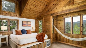 Ein Schlafzimmer einer Holzhütte mit Bett, Nachttisch, Lampe und einer Hängematte.