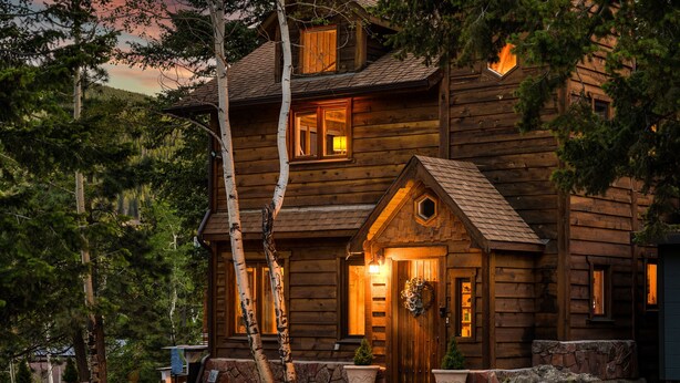 Eine rustikale Blockhütte mit Steinunterbau, einer Holztür und einer Veranda mit Blumentöpfen.