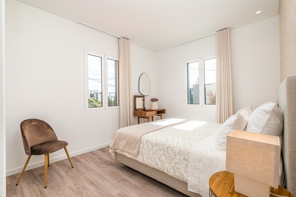 A bedroom with a bed, a chair, a nightstand, and a window.