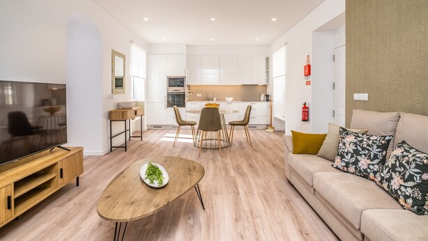 A modern living room with a flat-screen TV, wooden coffee table, and a sofa with floral cushions. - Casa Buganvília (Funchal)