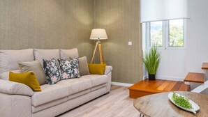 A modern living room with a beige sofa, a wooden coffee table, a floor lamp, and a potted plant. - Casa Buganvília (Funchal)