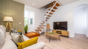 A modern living room with a staircase, a sofa, a coffee table, and a TV. - Casa Buganvília (Funchal)