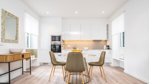 A modern kitchen with white cabinets, a round dining table, and two chairs. - Casa Buganvília (Funchal)