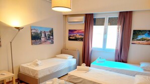 A hotel room with two single beds, a desk, a lamp, and two paintings on the wall. - Comfortable apartment in Syntagma square (Athina)