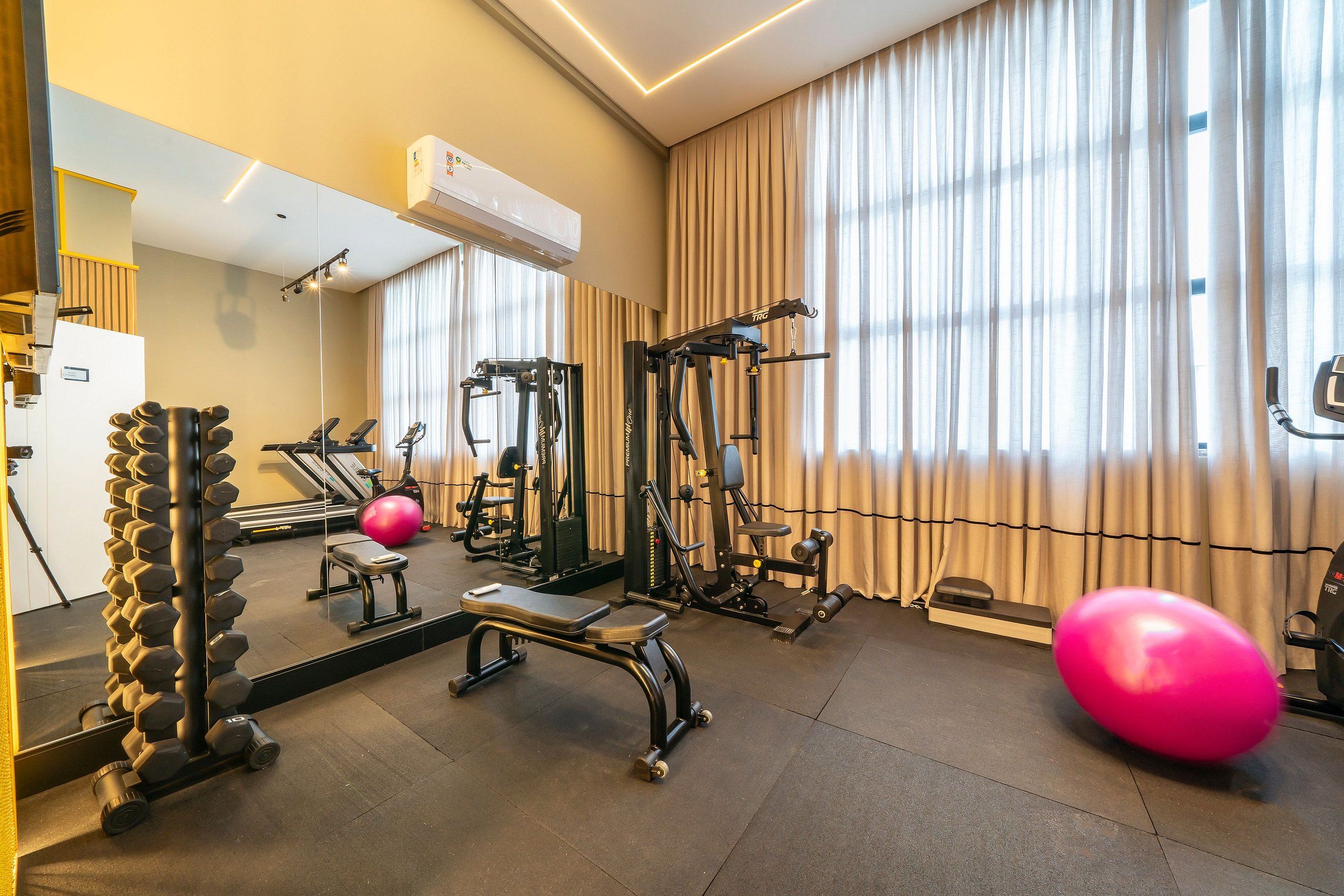 A gym with exercise equipment, a mirror, and a large window with curtains.