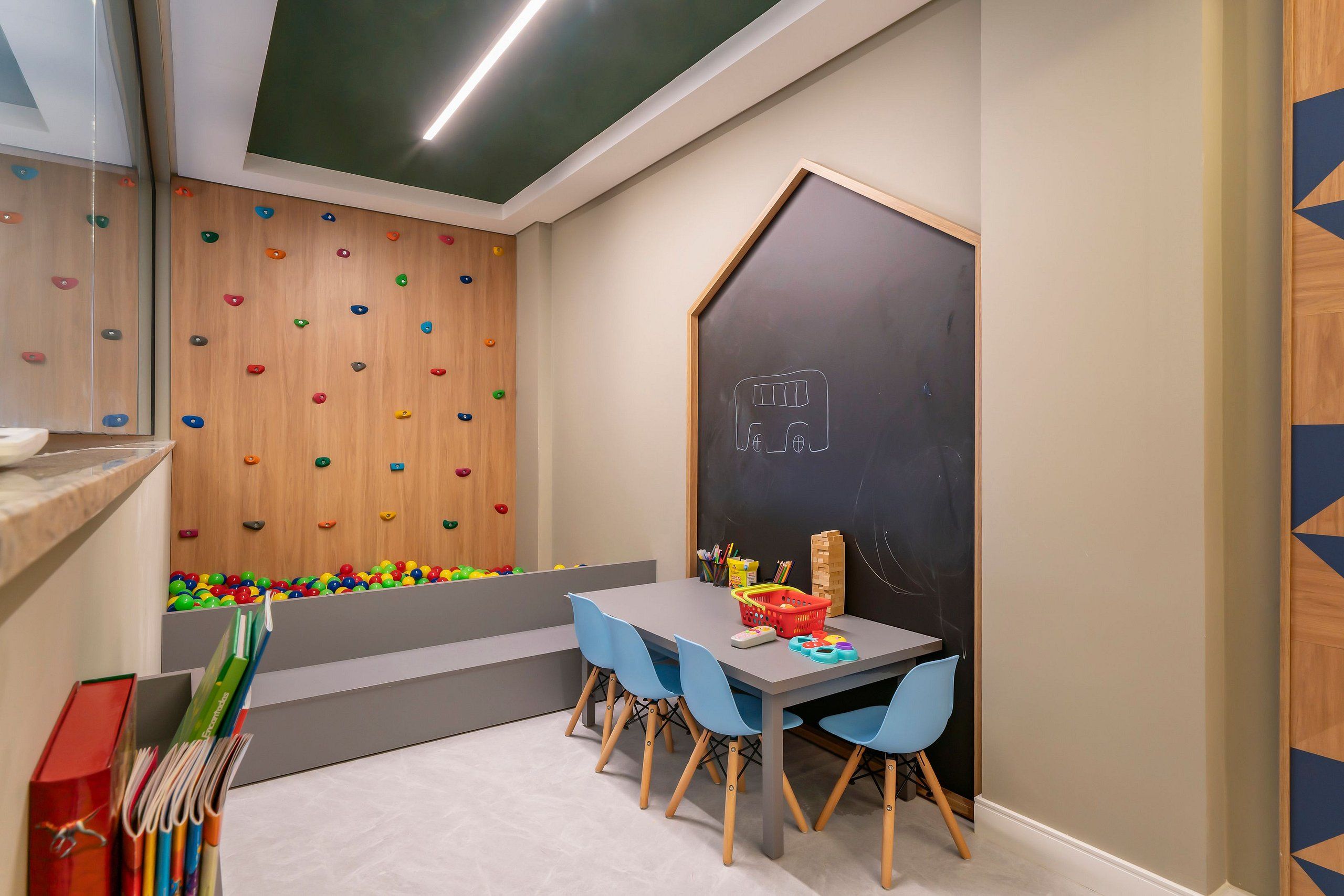A children's playroom with a climbing wall, a chalkboard, and a table with chairs.