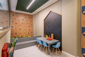 Un salón infantil con una pared de escalada, una pizarra y una mesa con sillas.