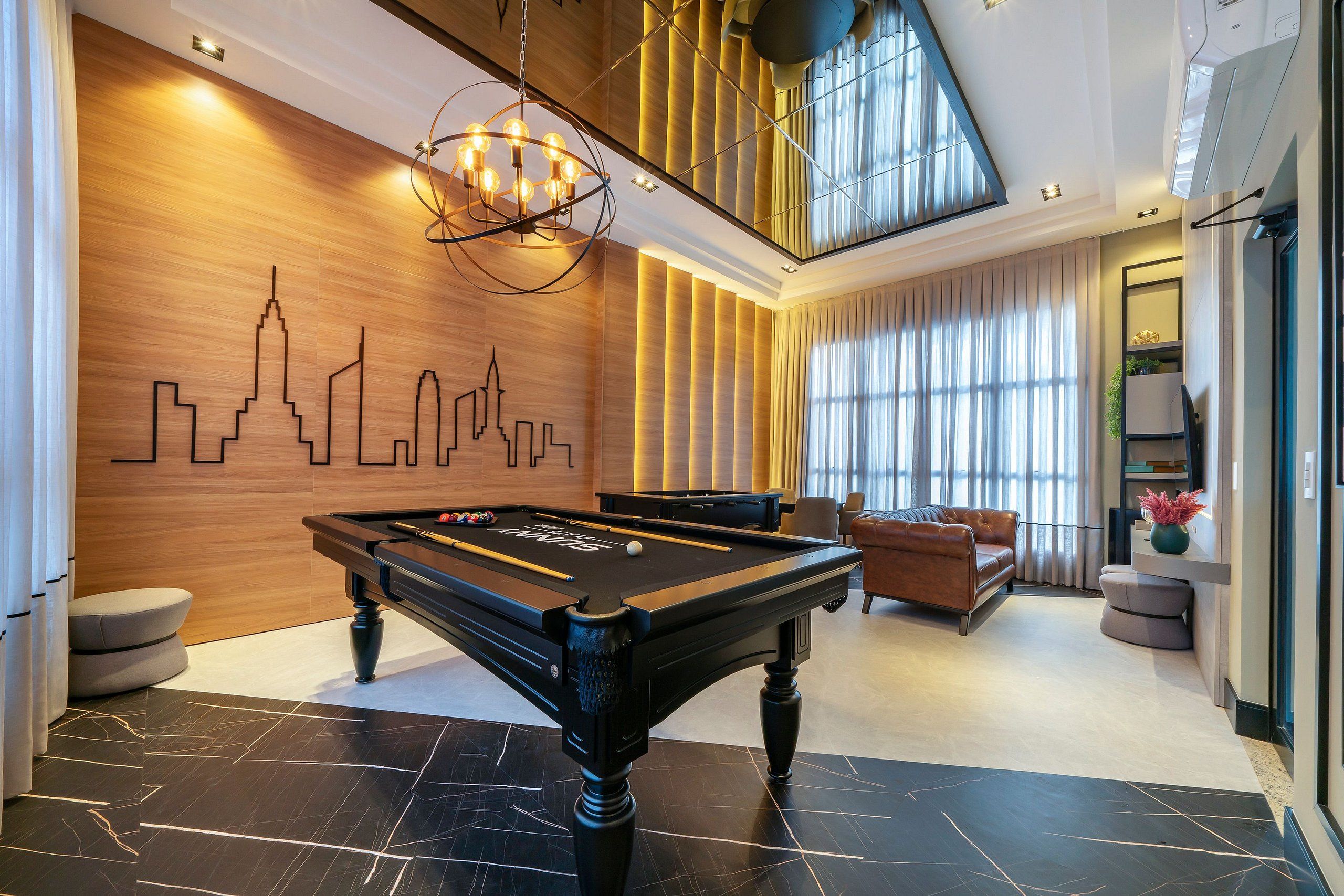 A modern indoor pool table with a city skyline mural, a lounge area with sofas, and a large window with curtains.