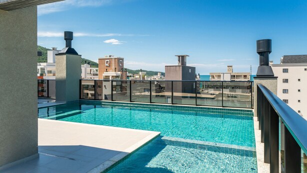 A rooftop swimming pool with clear blue water, surrounded by modern buildings and a view of a hilly landscape. - Sunny Flats  (Bombinhas)