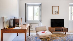 A living room with a wooden coffee table, a television on a wooden stand, a sofa, and a large window with curtains. - Atelier by the Sea (Porto)
